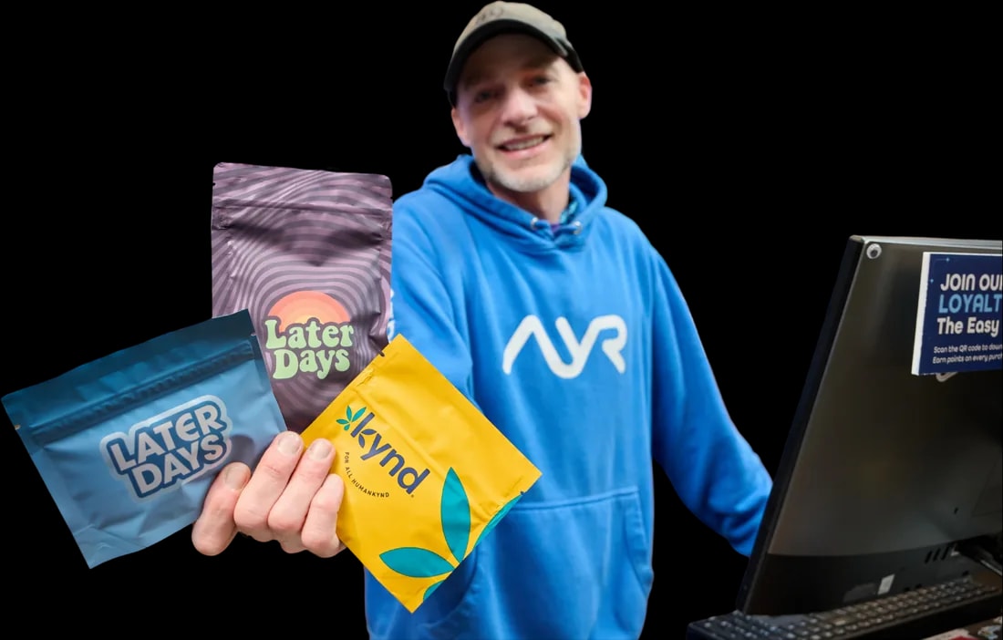 Ayr Budtender in a blue Ayr hoodie holding Later Days and kynd product pouches